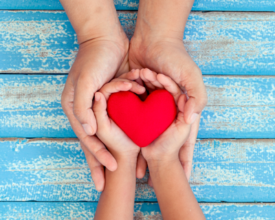 A pair of child's hands holds a red heart; an adult holds the child's hands.