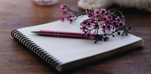 A pen and a flower rest on a journal